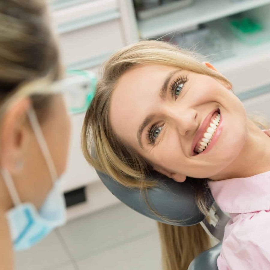 Horizontal color close-up headshot of beautiful woman having dental examination and sincerely smiling at dentist.